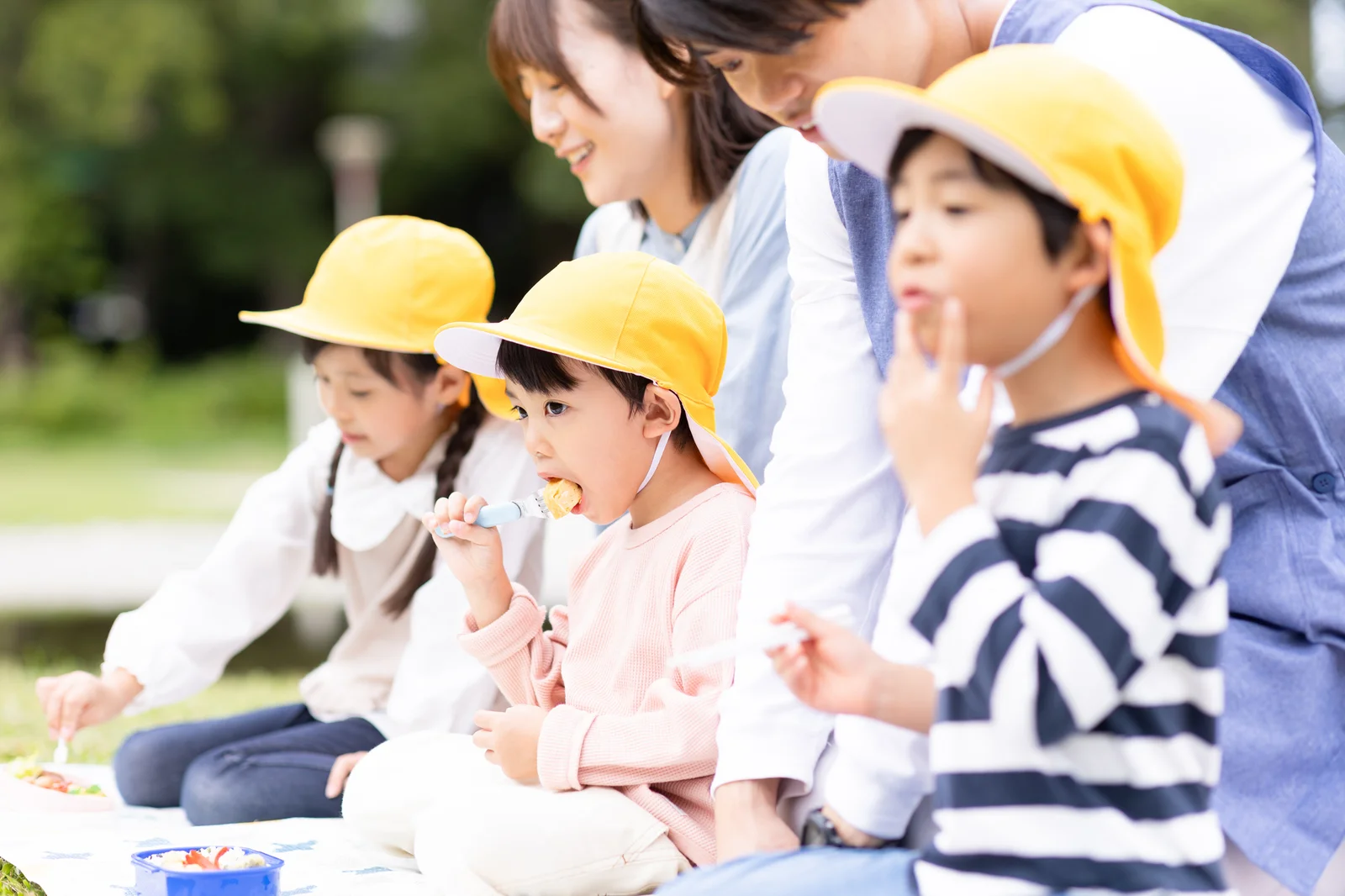 屋外で、スタッフと子どもたちが一緒に昼食をとっている様子